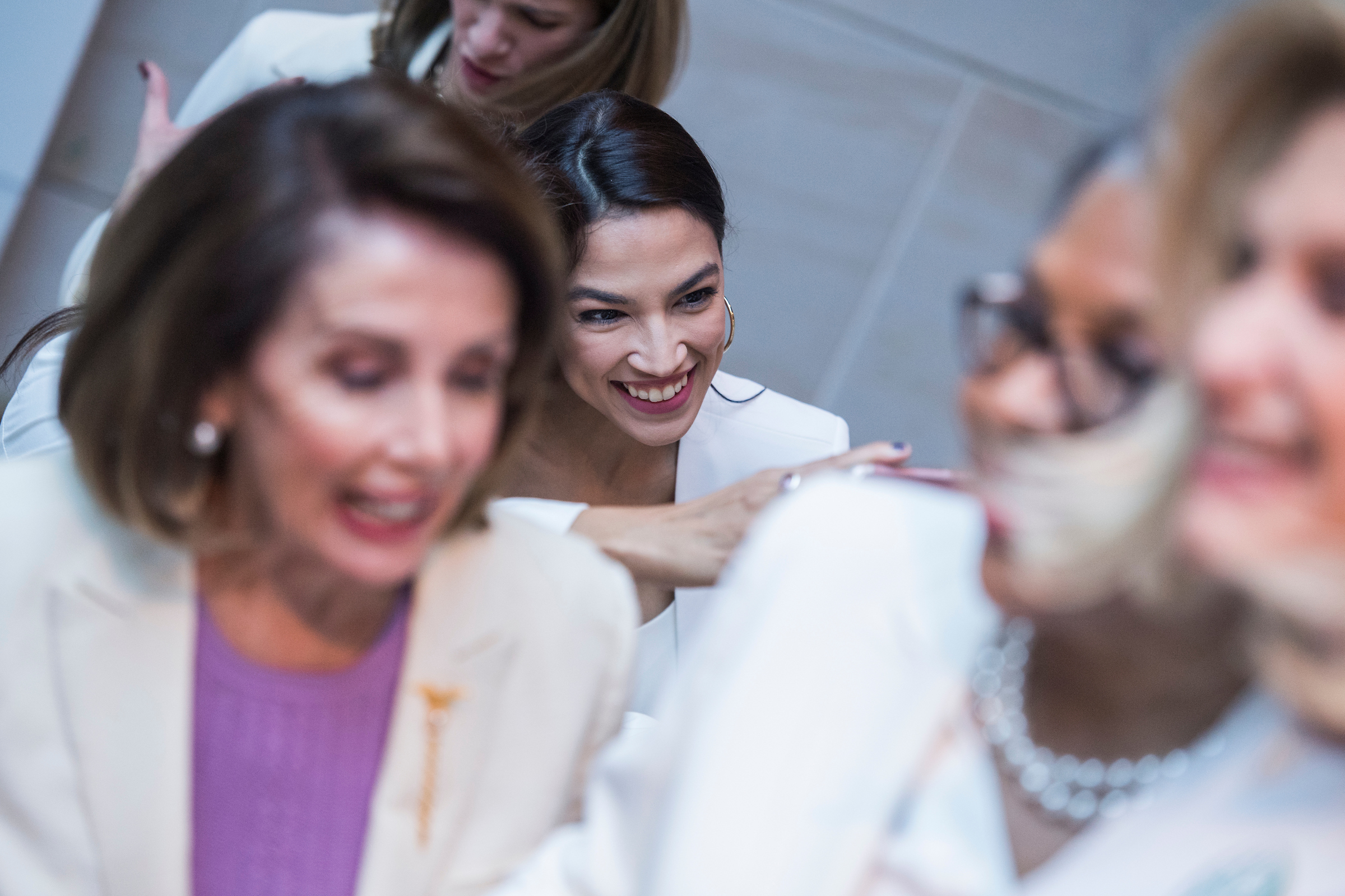 UNITED STATES - FEBRUARY 05: Rep. Alexandria Ocasio-Cortez, D-N.Y., center, and Speaker Nancy Pelosi, D-Calif., left, pose for a group photo of House Democrats in the Capitol Visitor Center, who plan to wear "suffragette white" to the State of the Union address to show solidarity for women's agendas on Tuesday, February 5, 2019. (Photo By Tom Williams/CQ Roll Call)
