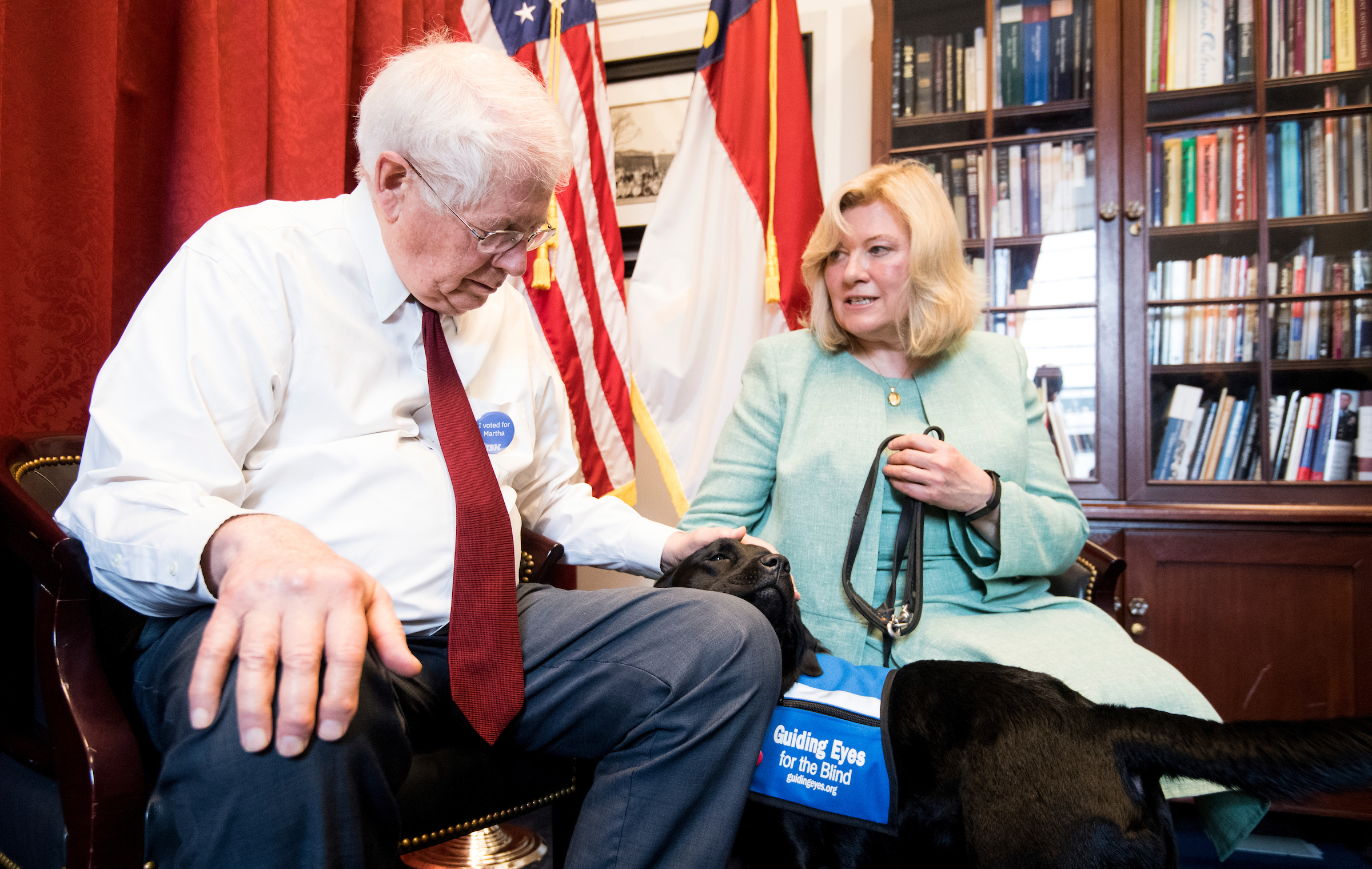 UNITED STATES - MAY 1: Volunteer puppy raiser Lorraine Trapani speaks with Rep. David Price, D-N.C., as he pets Kate, a 14 month old black labrador retriever in the Guiding Eyes for the Blind training program, in his office on Wednesday, May 1, 2019. Kate is wearing a 