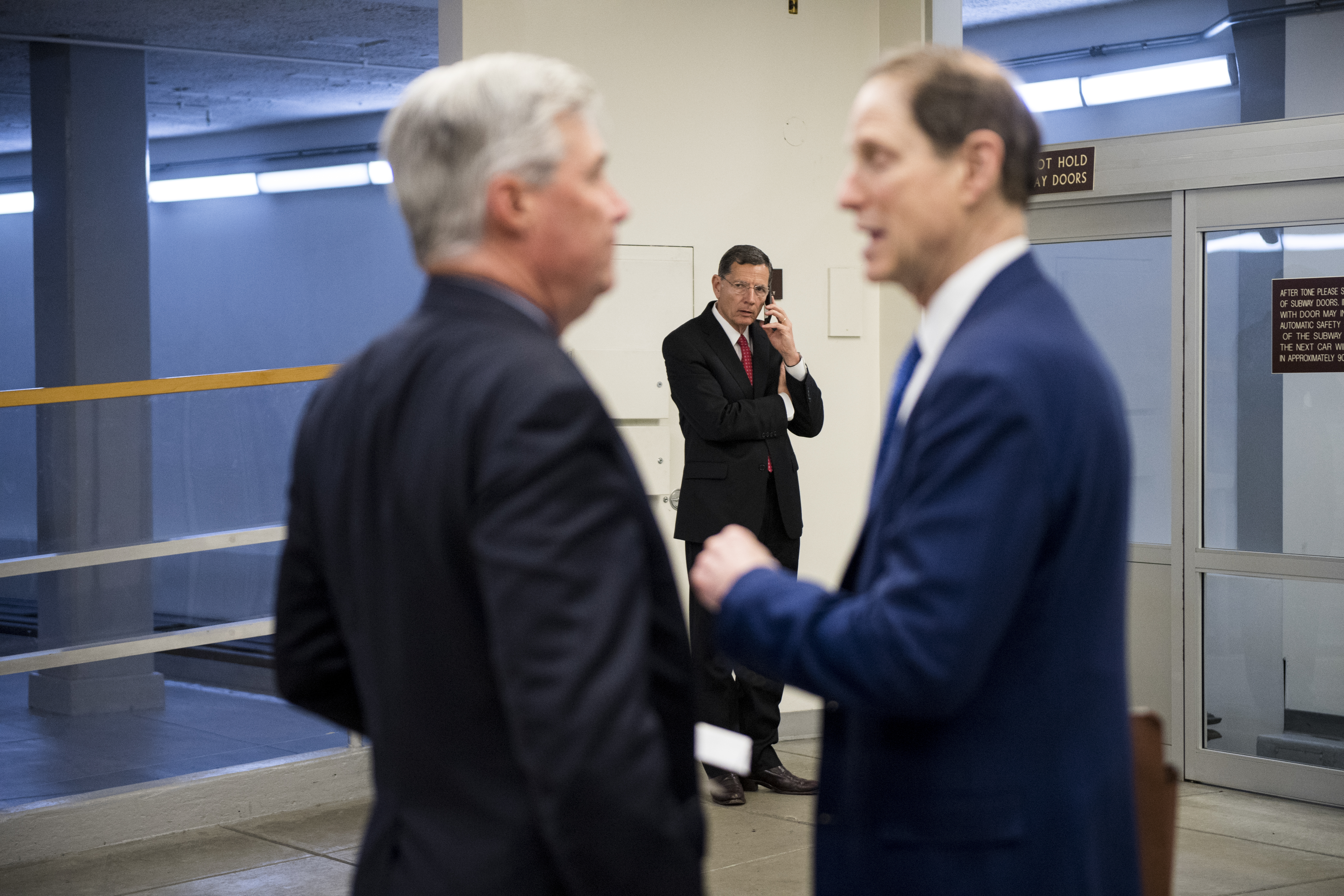 UNITED STATES - JUNE 18: Sen. John Barrasso, R-Wyo., center, talks on his phone as Sen. Sheldon Whitehouse, D-R.I., left, and Sen. Ron Wyden, D-Ore., talk at the Senate subway in the Capitol on Tuesday, June 18, 2019. (Photo By Bill Clark/CQ Roll Call)