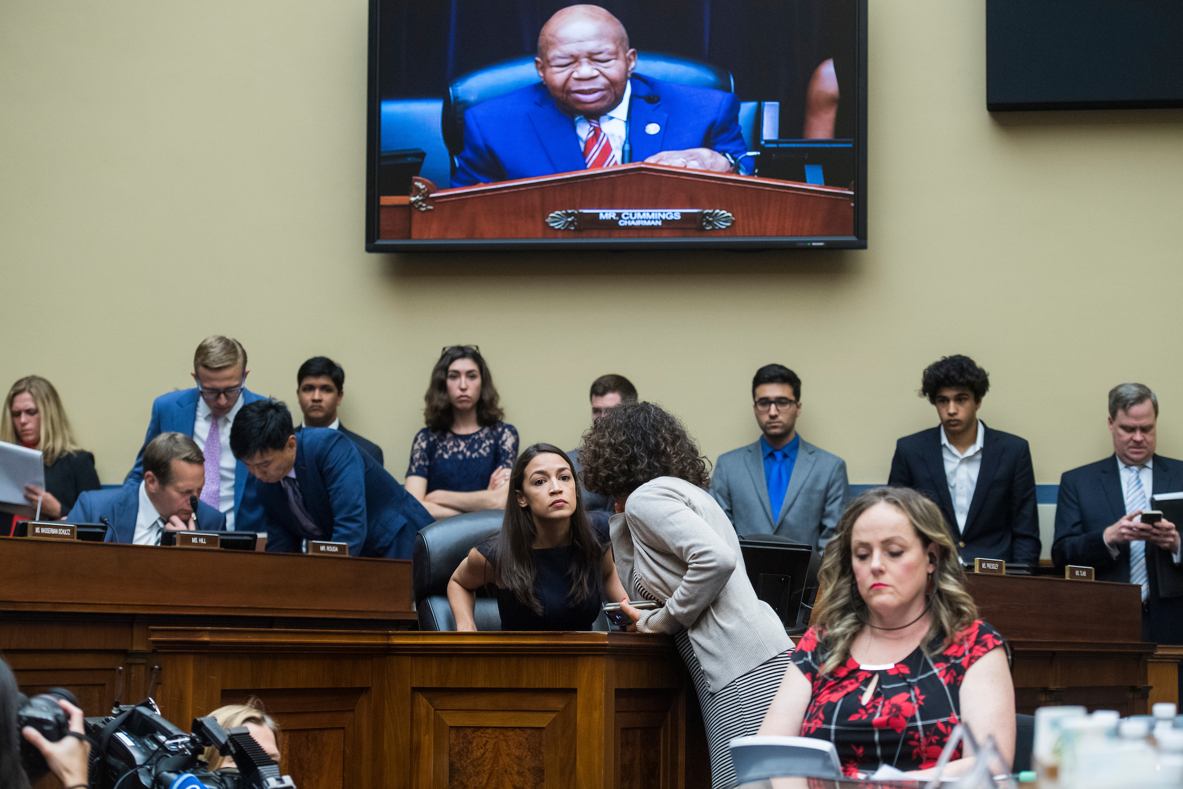 House Oversight and Reform Committee Chairman Elijah Cummings, D-Md., is seen on a monitor as Rep. Alexandria Ocasio-Cortez, D-N.Y., talks with an aide during a committee meeting on July 12, 2019. A new Oversight filing in D.C. court pushes back on a Trump administration strategy to stymie congressional investigations by limiting the scope of what they can seek from the White House. (Tom Williams/CQ Roll Call file photo)