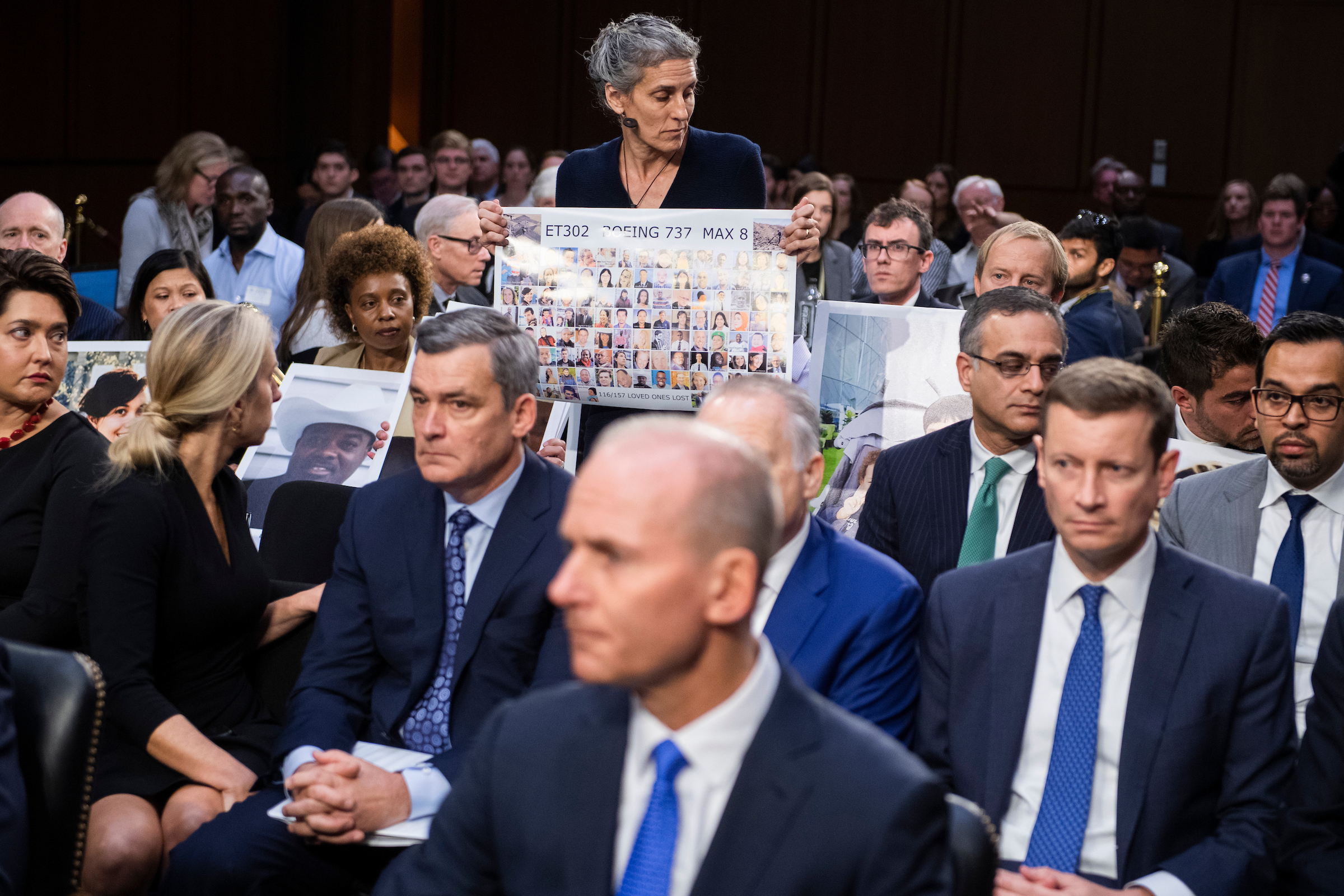 Nadia Milleron, whose daughter Samya Stumo was killed in the crash of Ethiopian Airlines Flight 302, holds a sign with victims of the crash Tuesday behind Boeing CEO Dennis Muilenburg, foreground, during the Senate Commerce, Science and Transportation Committee hearing on aviation safety and the future of the Boeing 737 MAX. (Tom Williams/CQ Roll Call)