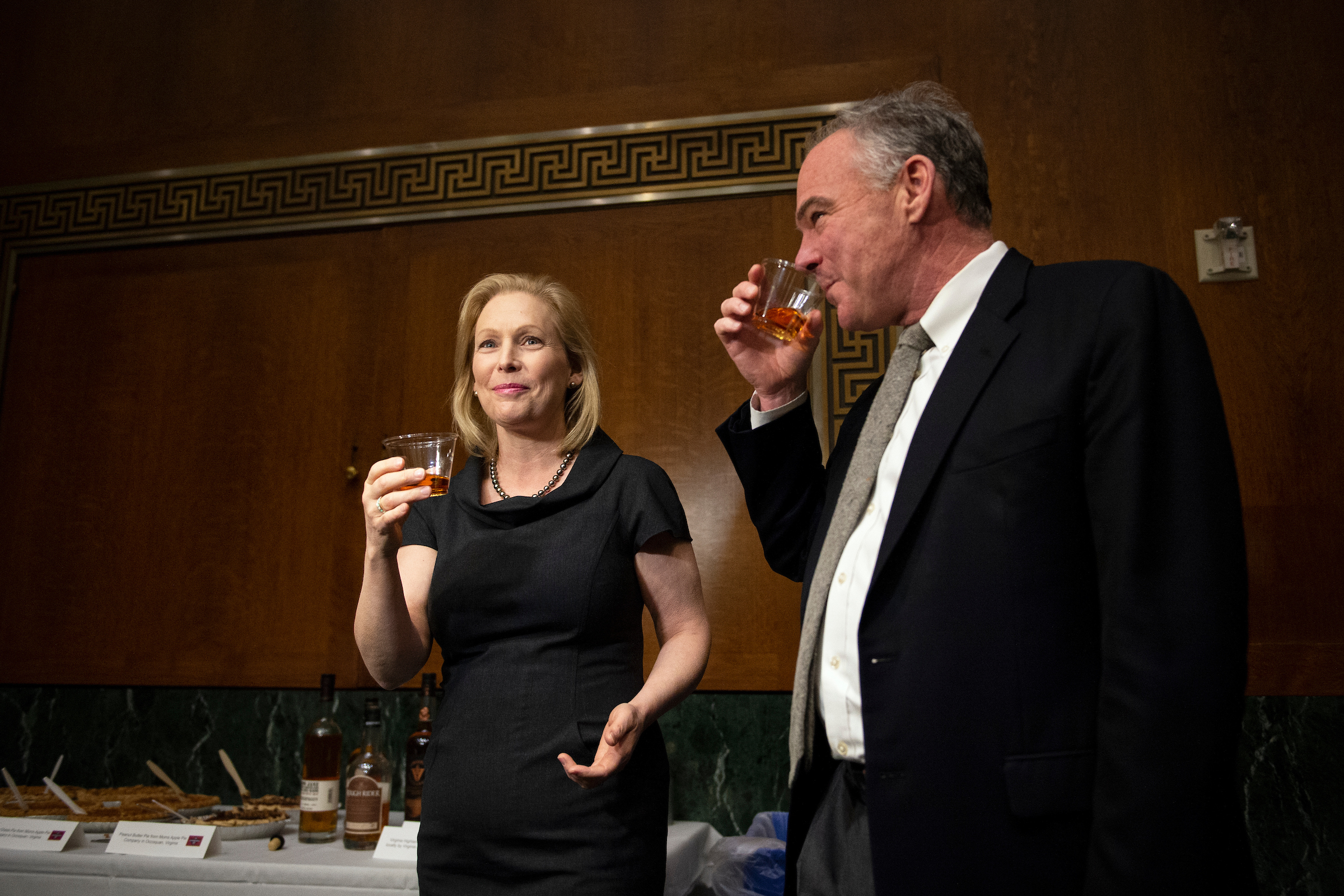UNITED STATES - DECEMBER 5: Sen. Kirsten Gillibrand, D-N.Y., left, shares a drink of New York whiskey with Sen. Tim Kaine, D-Va., at the Capitol on Thursday Dec. 5, 2019. Sen. Kirsten Gillibrand, D-N.Y., placed a ALCS bet with Sen. Ted Cruz, R-Texas. As the loser, Sen. Kirsten Gillibrand, D-N.Y., provided New York themed desserts for her and Cruz’s staffers. (Photo by Caroline Brehman/CQ Roll Call)