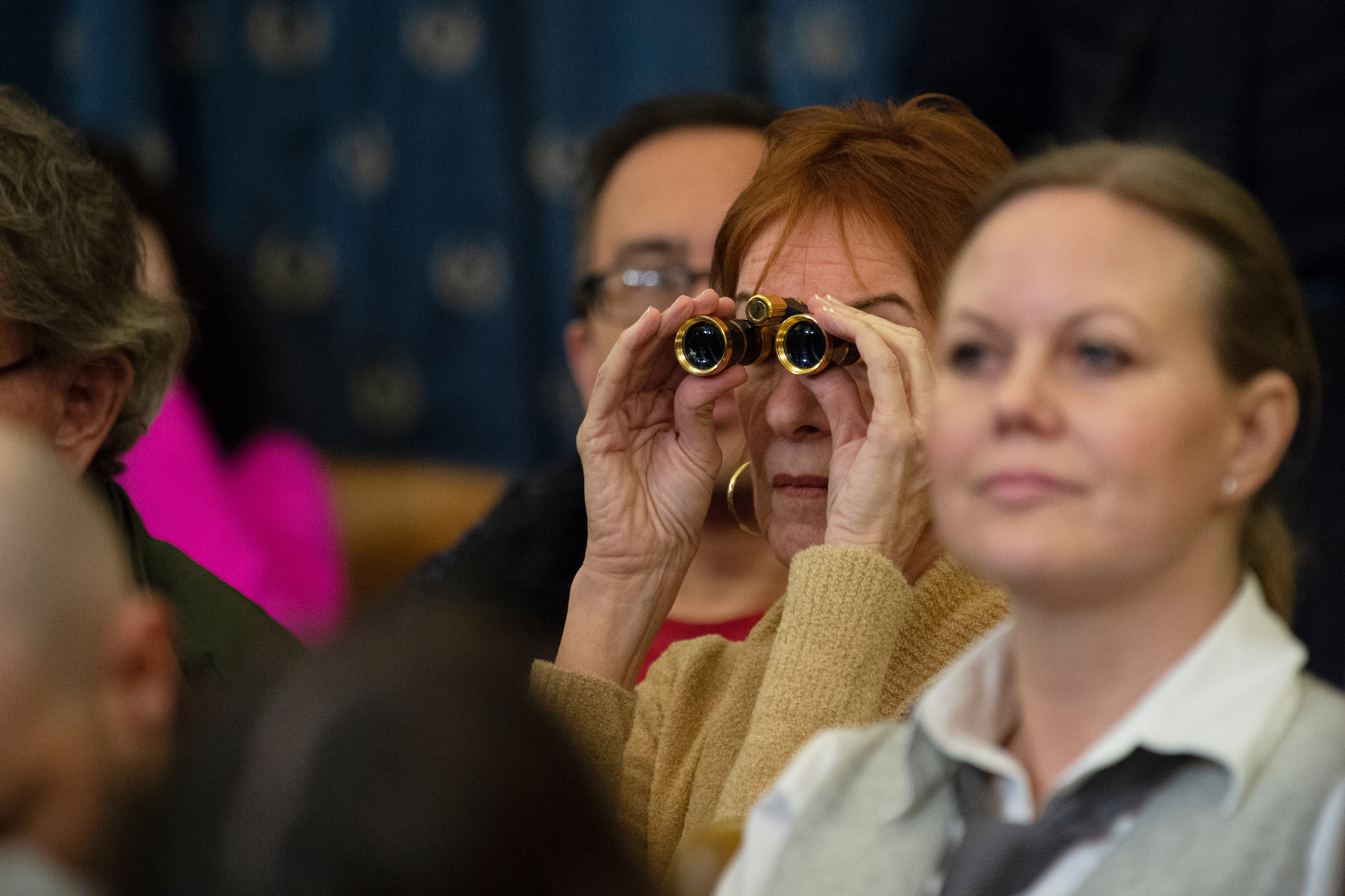 2020 vision?: A spectator uses binoculars Wednesday to watch the House Judiciary impeachment hearing. (Caroline Brehman/CQ Roll Call)